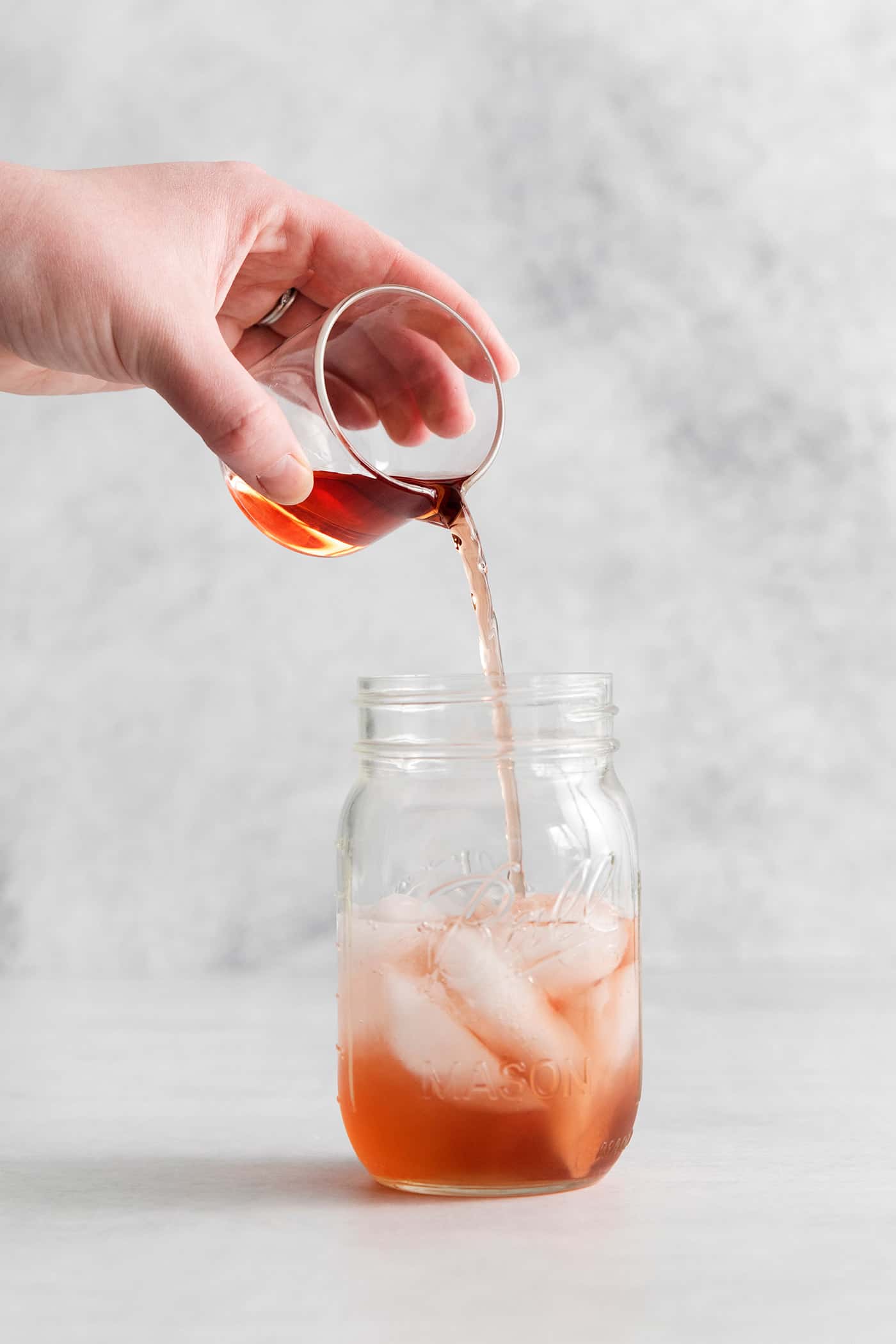 A hand pouring cranberry juice into a mason jar