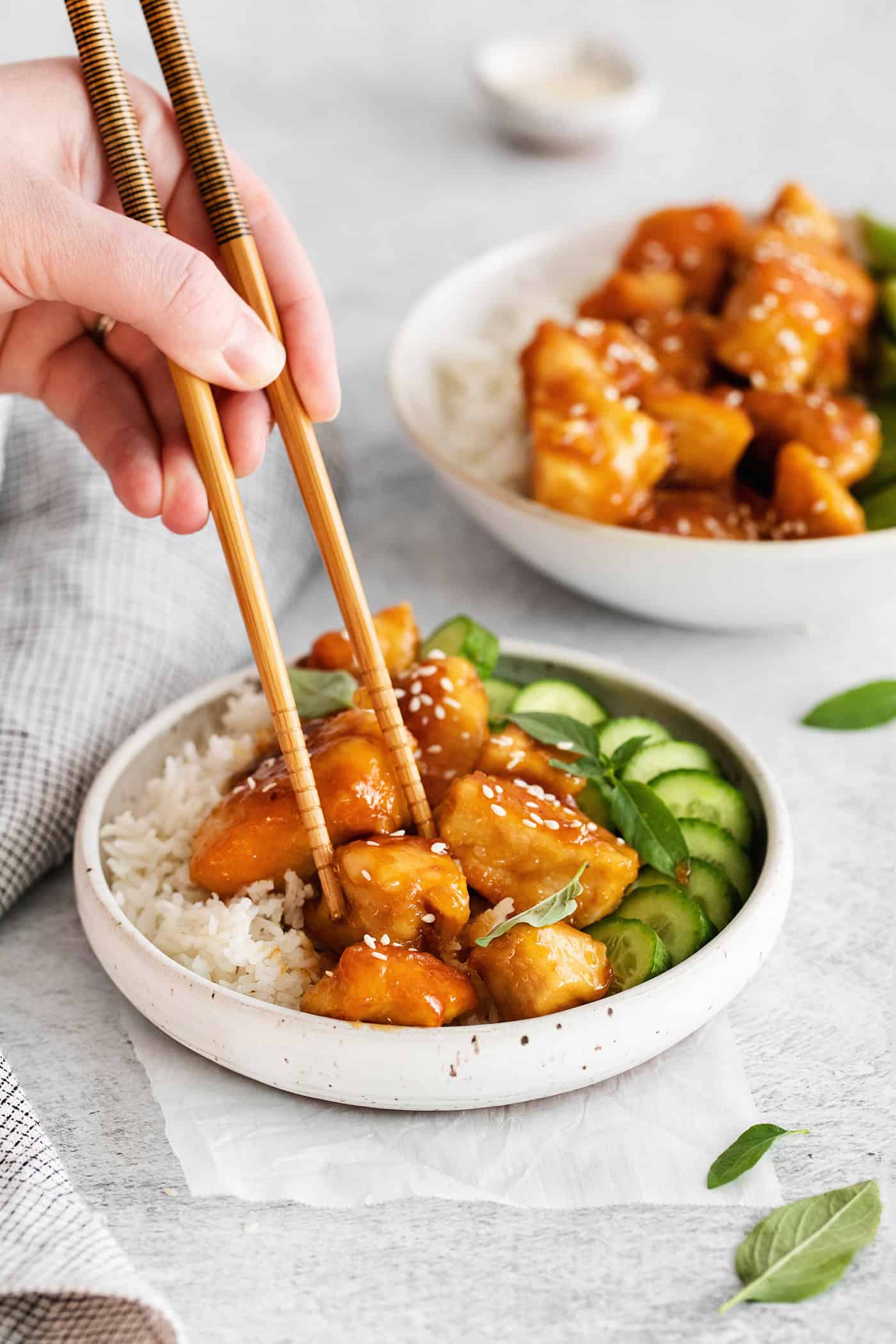 Chopsticks grabbing a piece of honey garlic chicken from a rice bowl