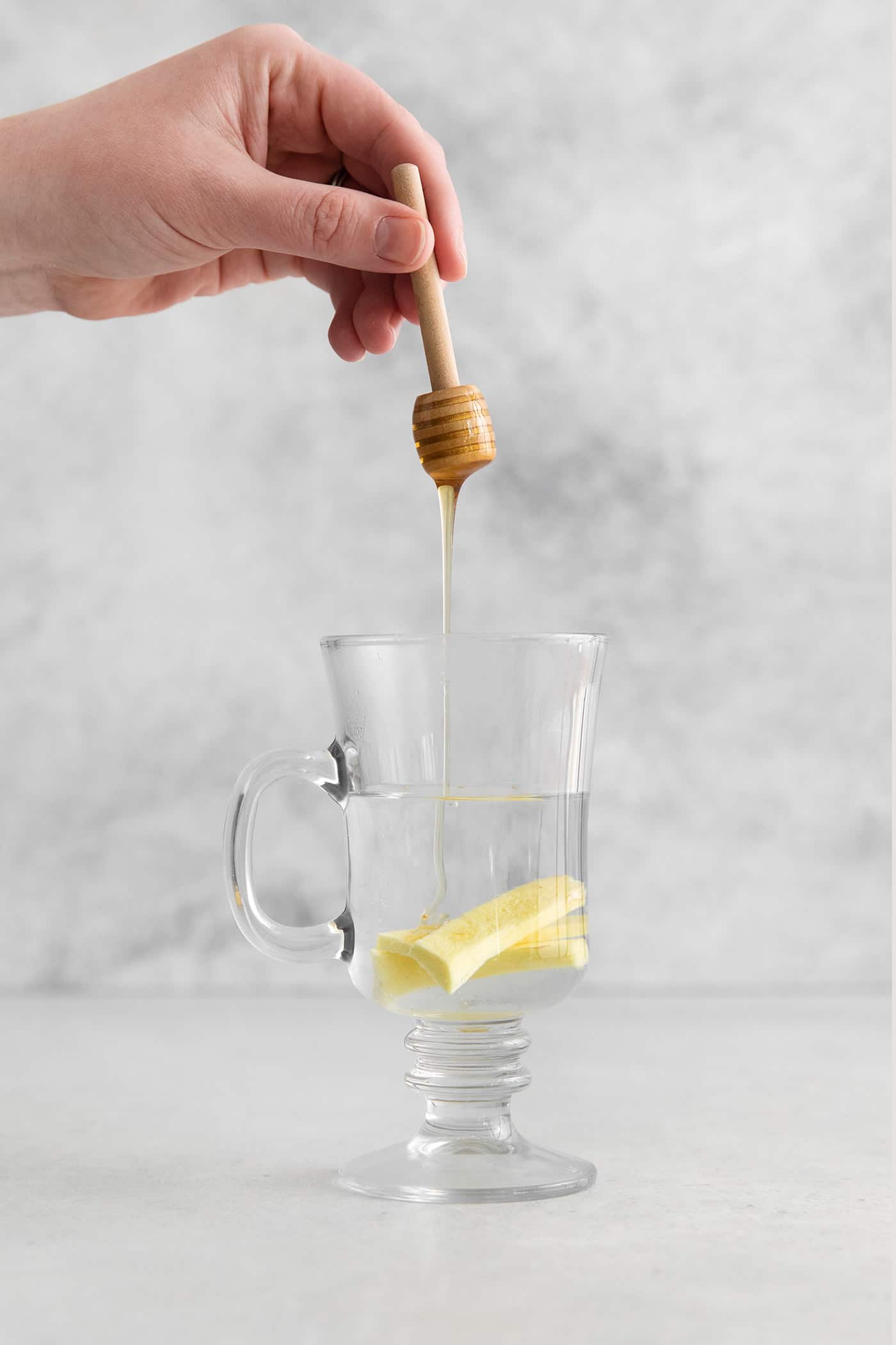 Honey being drizzled into a mug with hot water and ginger