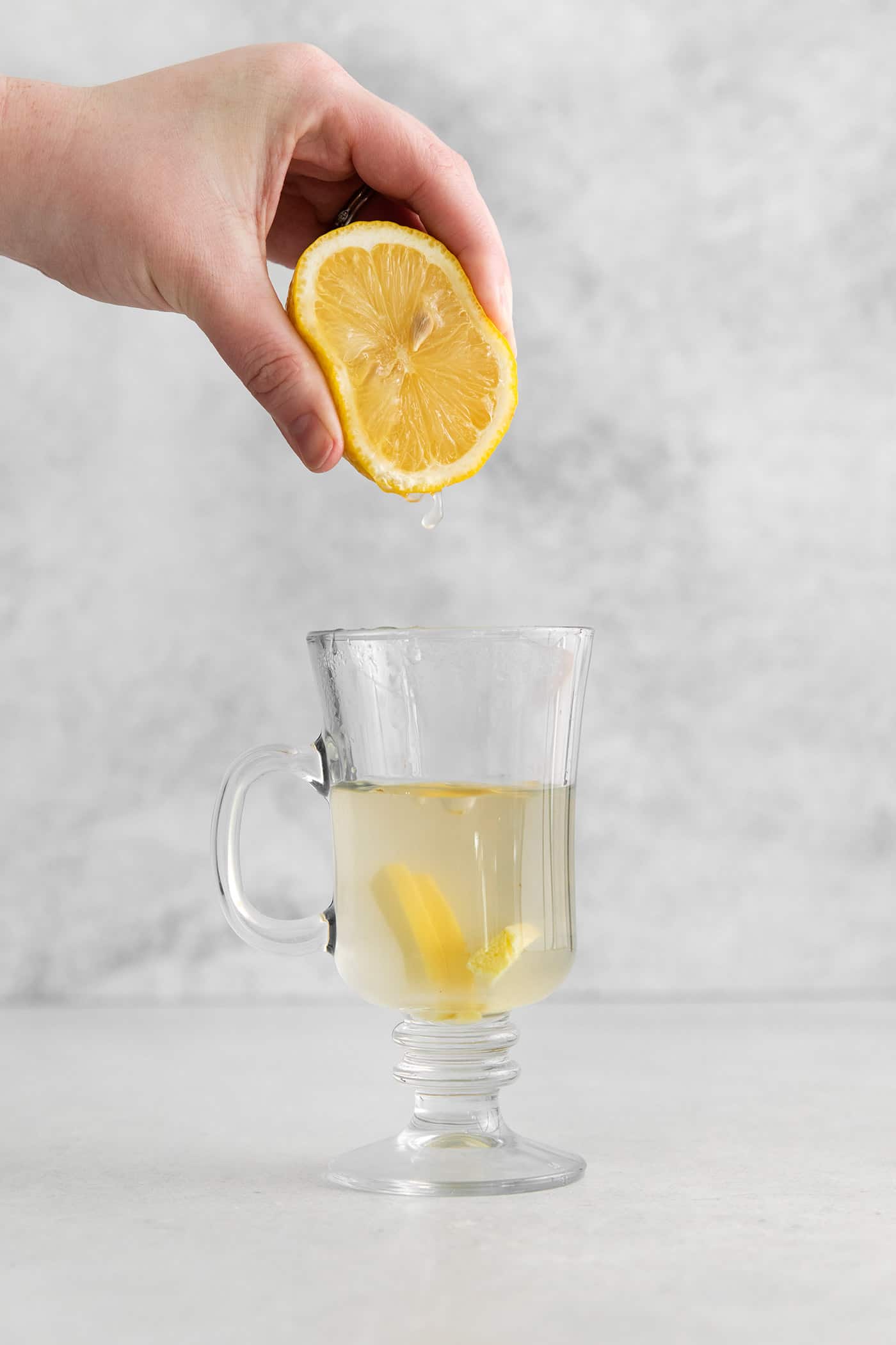 Lemon being squeezed into a mug of hot water and honey