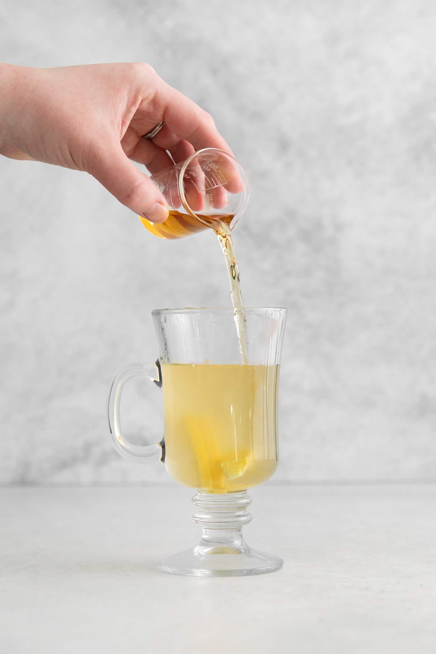 Bourbon being poured into a glass mug with lemon honey water