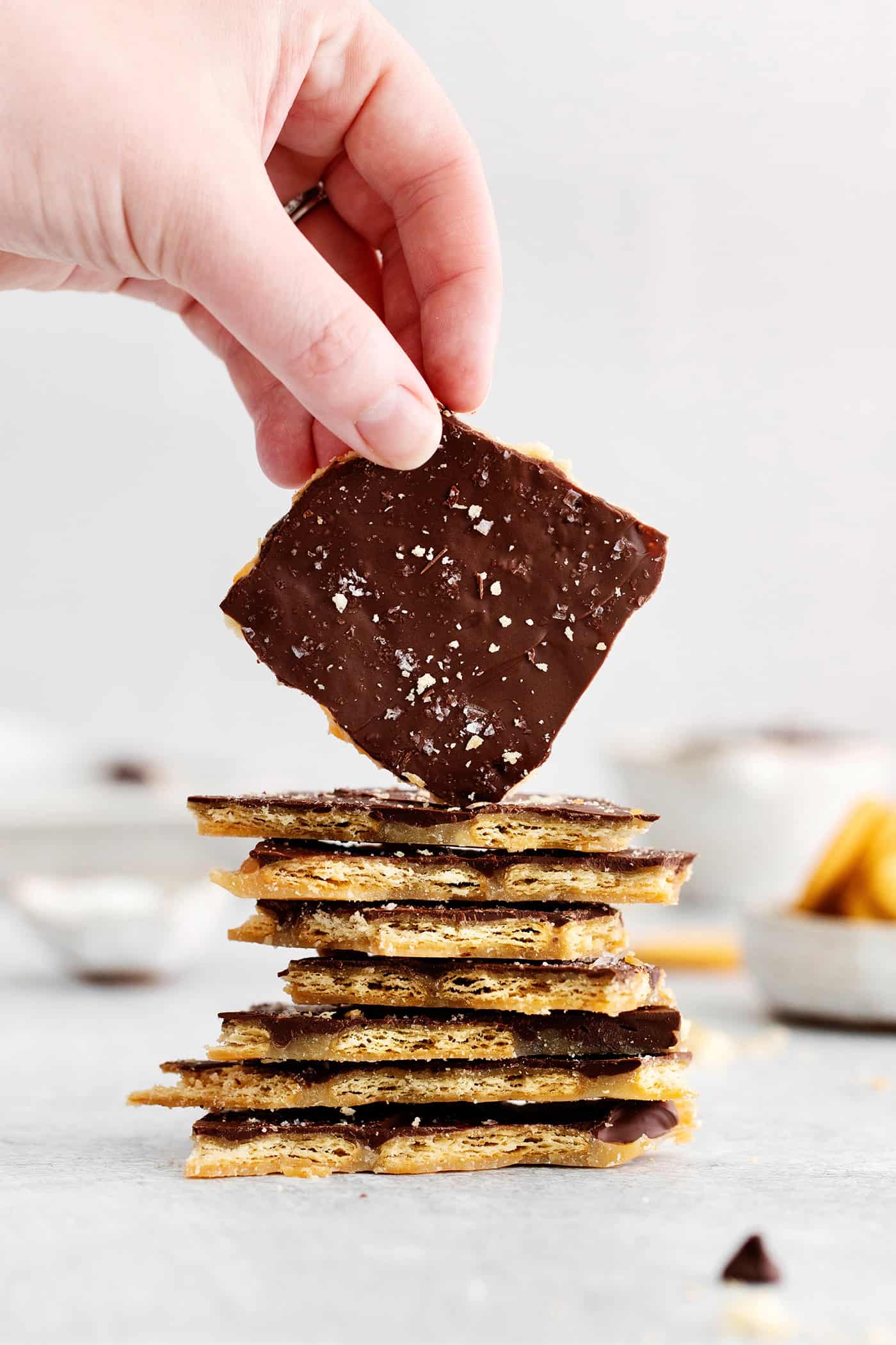 a stack of Ritz cracker toffee, with a hand holding up a piece