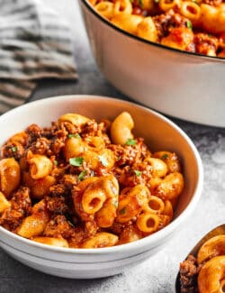 a bowl of beefaroni next to a large pot full of it