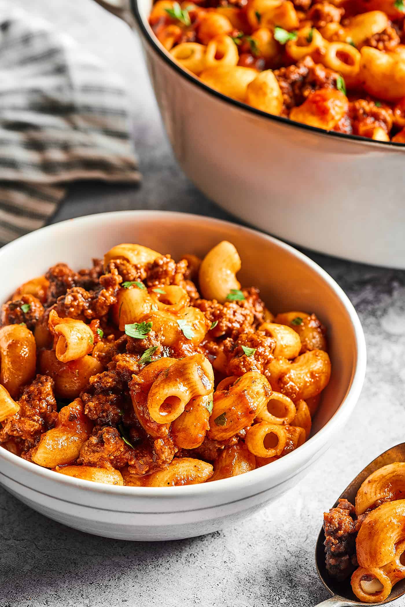 a bowl of beefaroni next to a large pot full of it