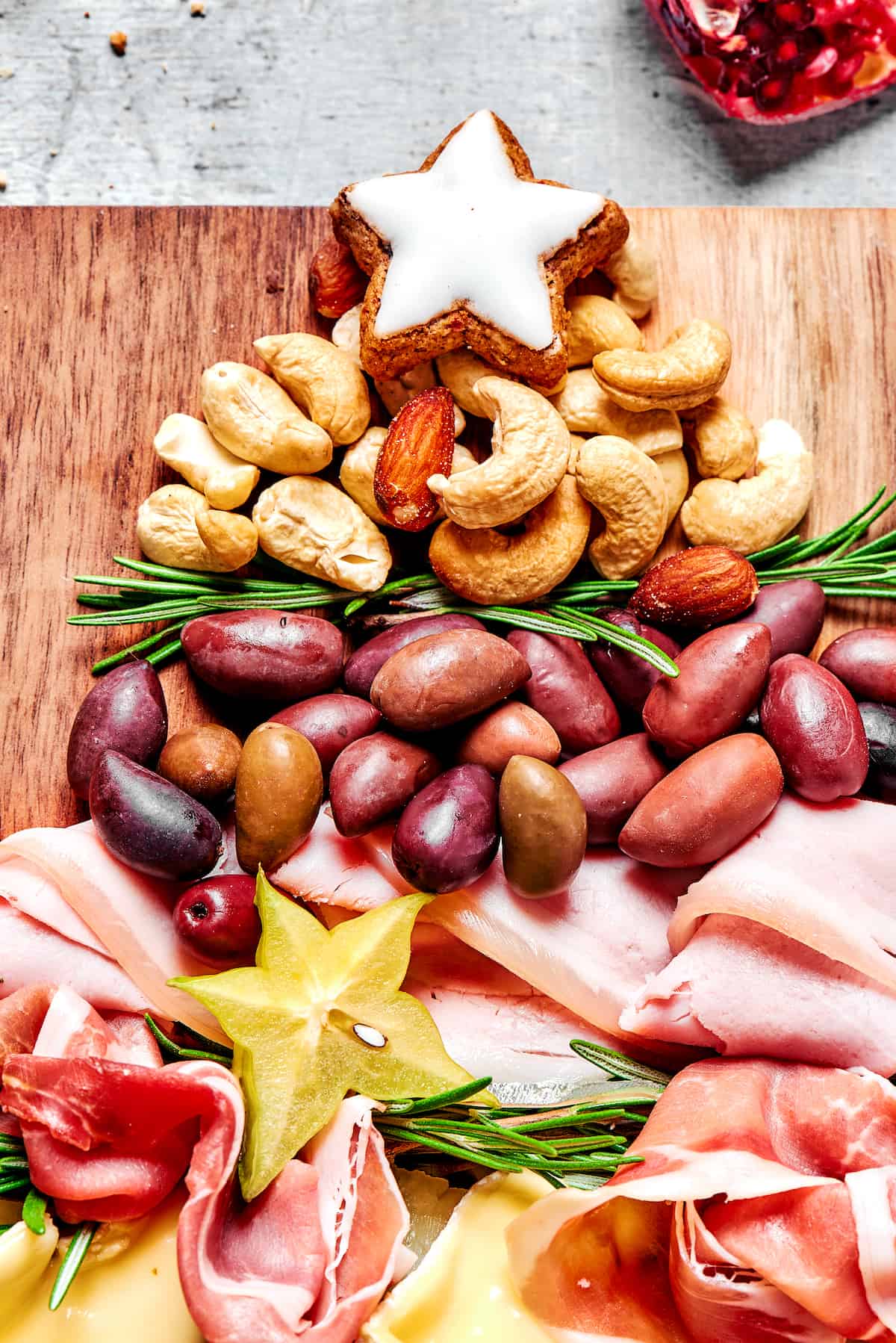 A cheese star, nuts, rosemary, olives, and ham on cutting board