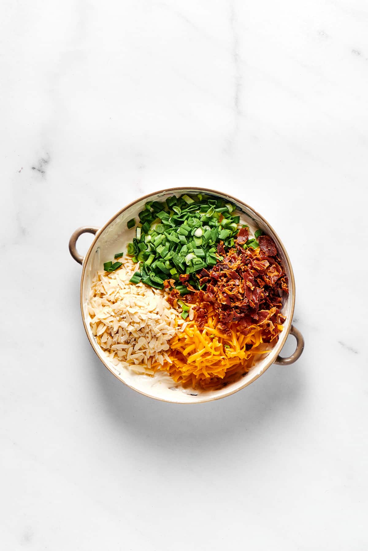 Green onions, almonds, cheddar cheese, and bacon in a bowl.