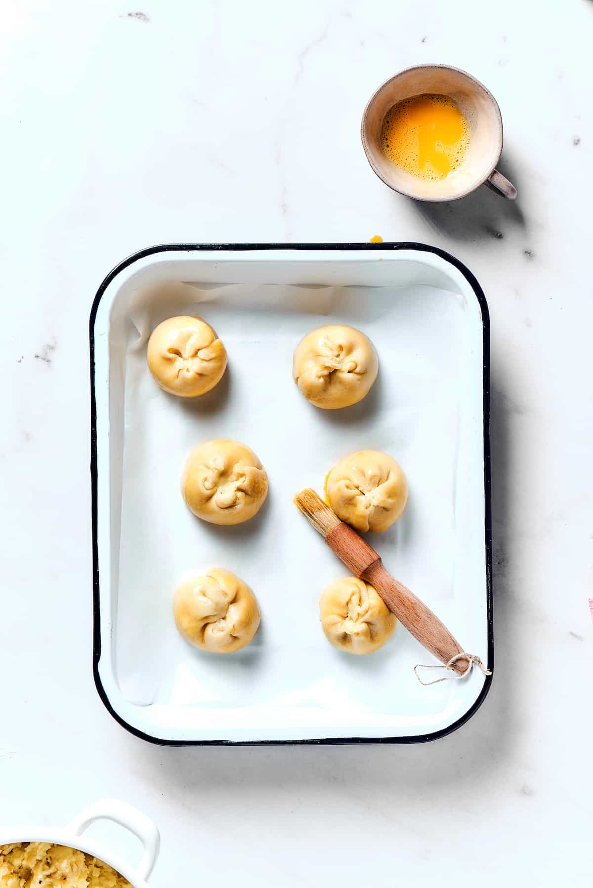 Butter being brushed on uncooked knish