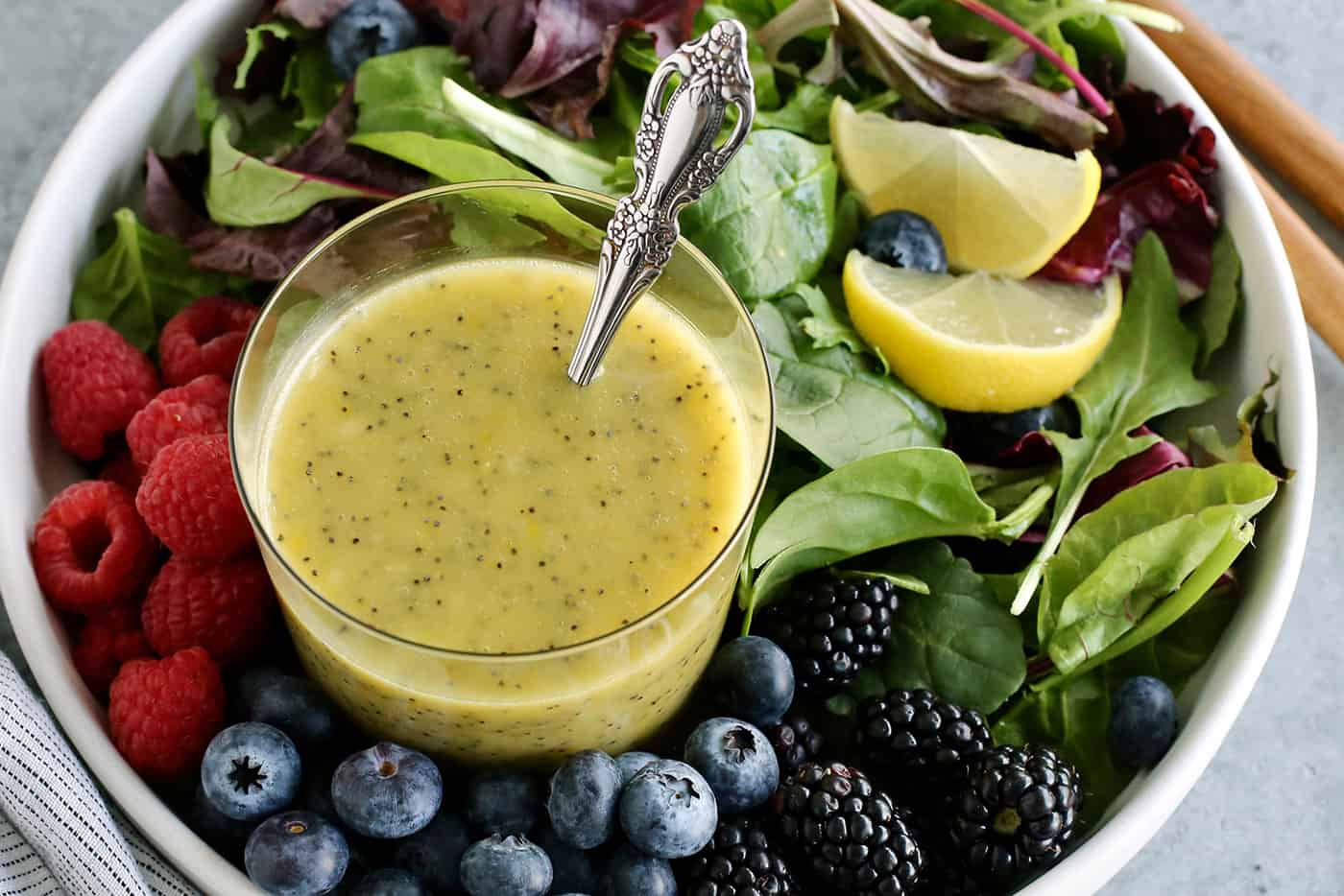 a cup of poppy seed dressing in a bowl of fresh greens and berries