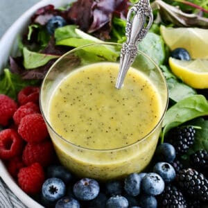 a cup of poppy seed dressing in a bowl of fresh greens and berries