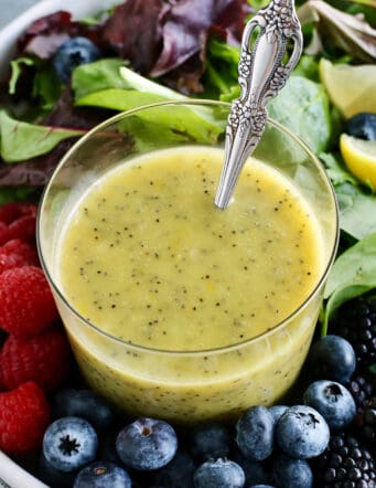 a cup of poppy seed dressing in a bowl of fresh greens and berries
