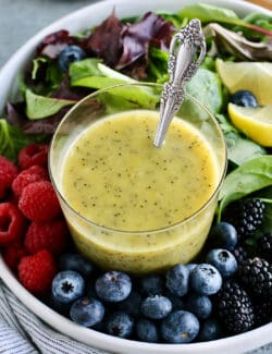 a cup of lemon poppy seed dressing and a bowl of fresh greens and berries