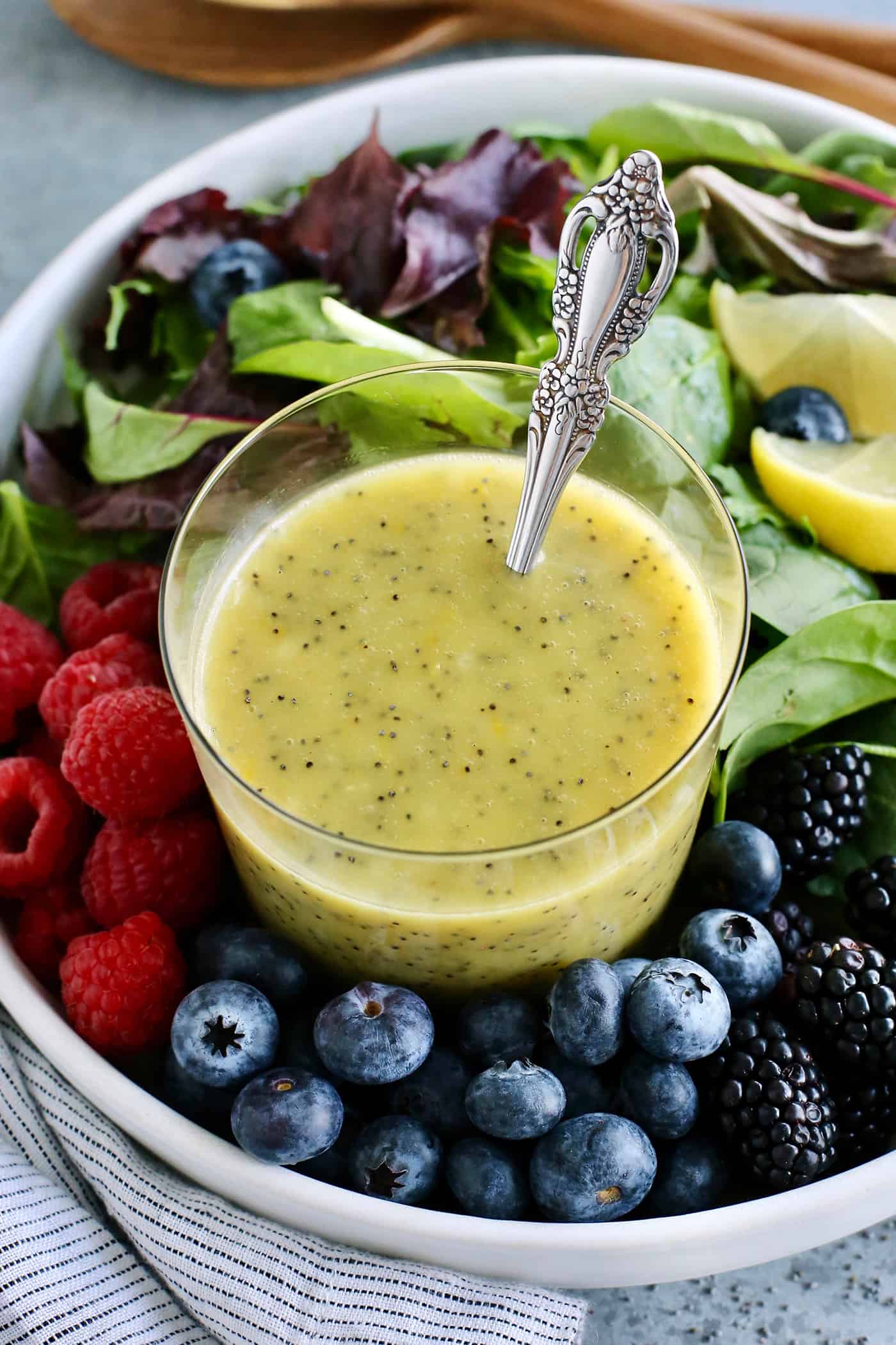 a cup of lemon poppy seed dressing and a bowl of fresh greens and berries