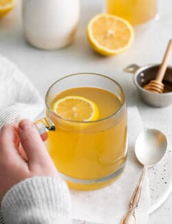 A hand holding a mug of medicine ball tea with lemon slices