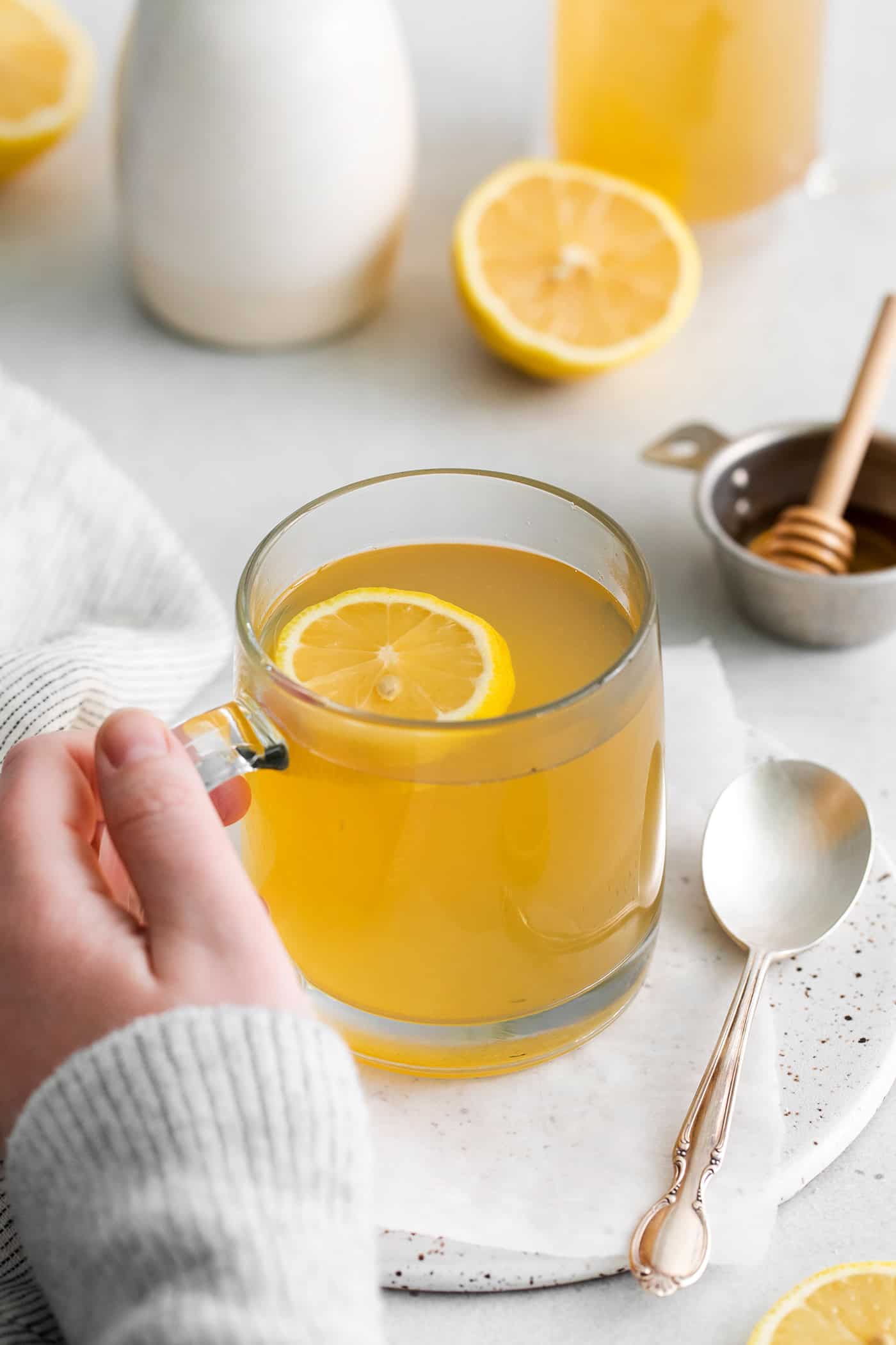 A hand holding a mug of medicine ball tea with lemon slices