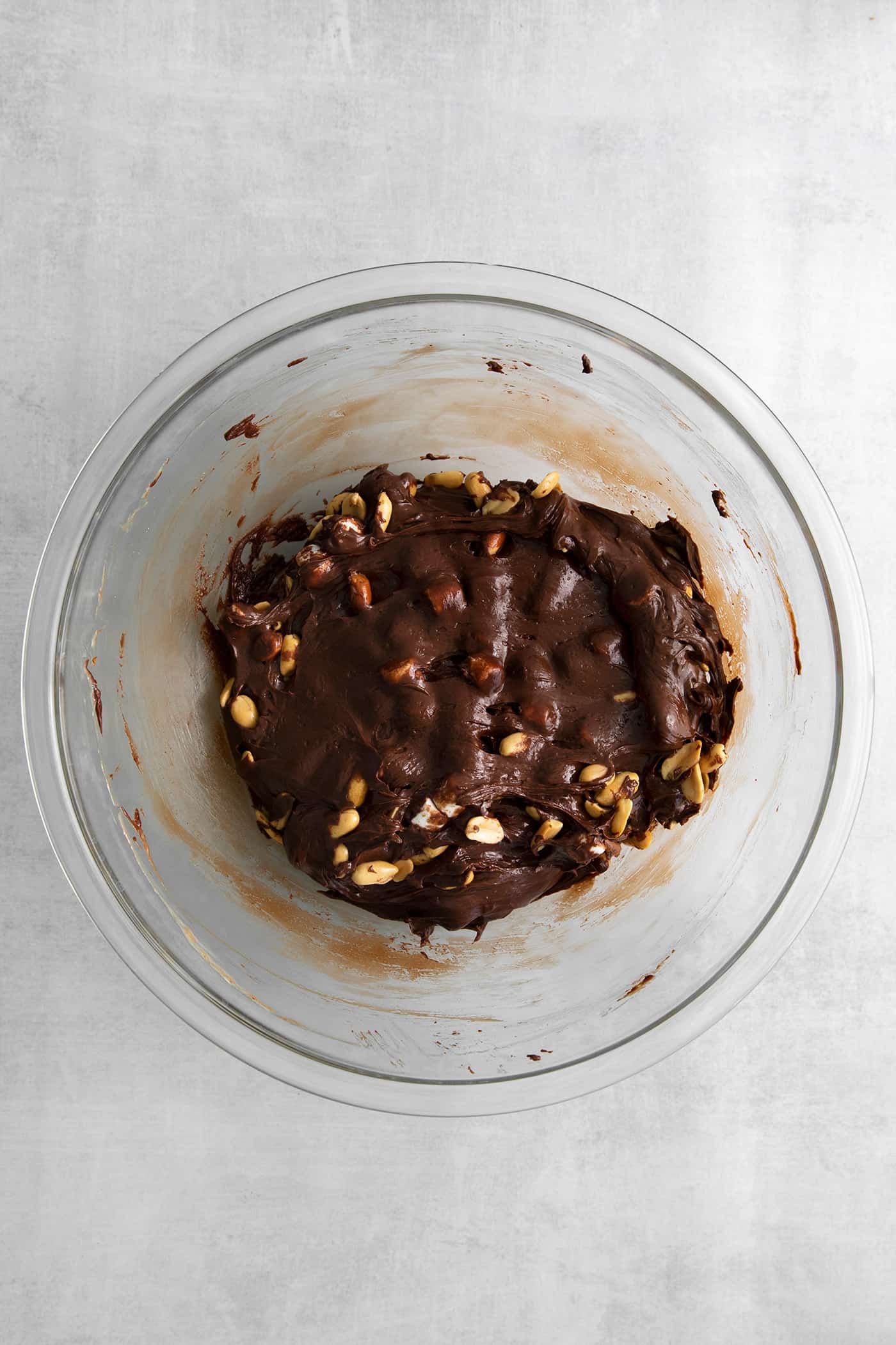 chocolate fudge mixture with peanuts and marshmallows in a clear mixing bowl