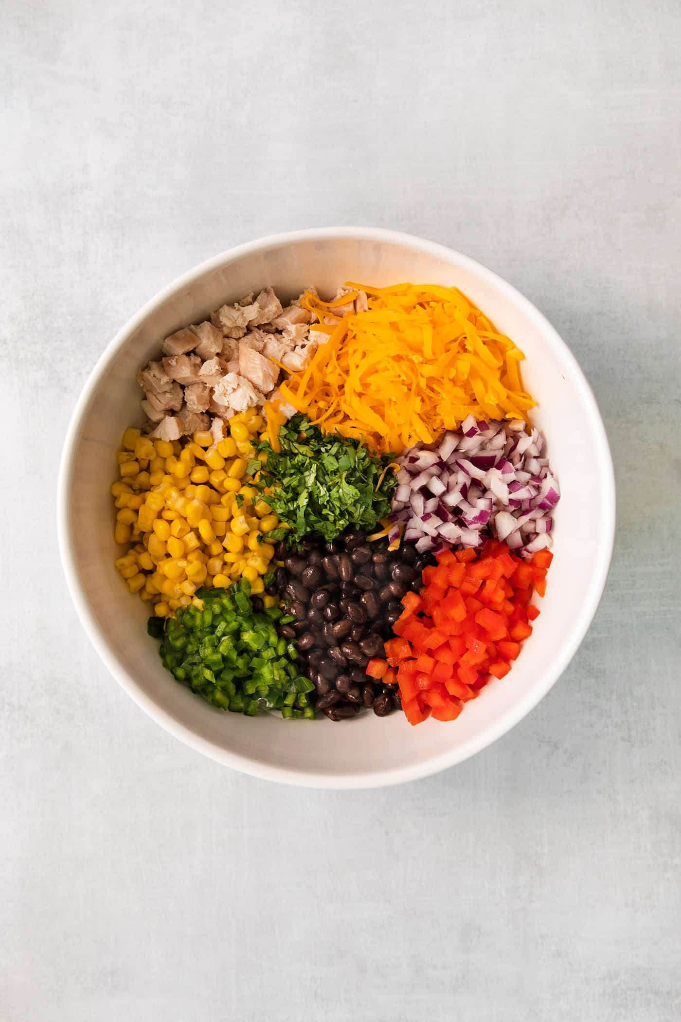 Chicken, cheese, onions, bell peppers, cilantro, and beans, and corn in a white bowl