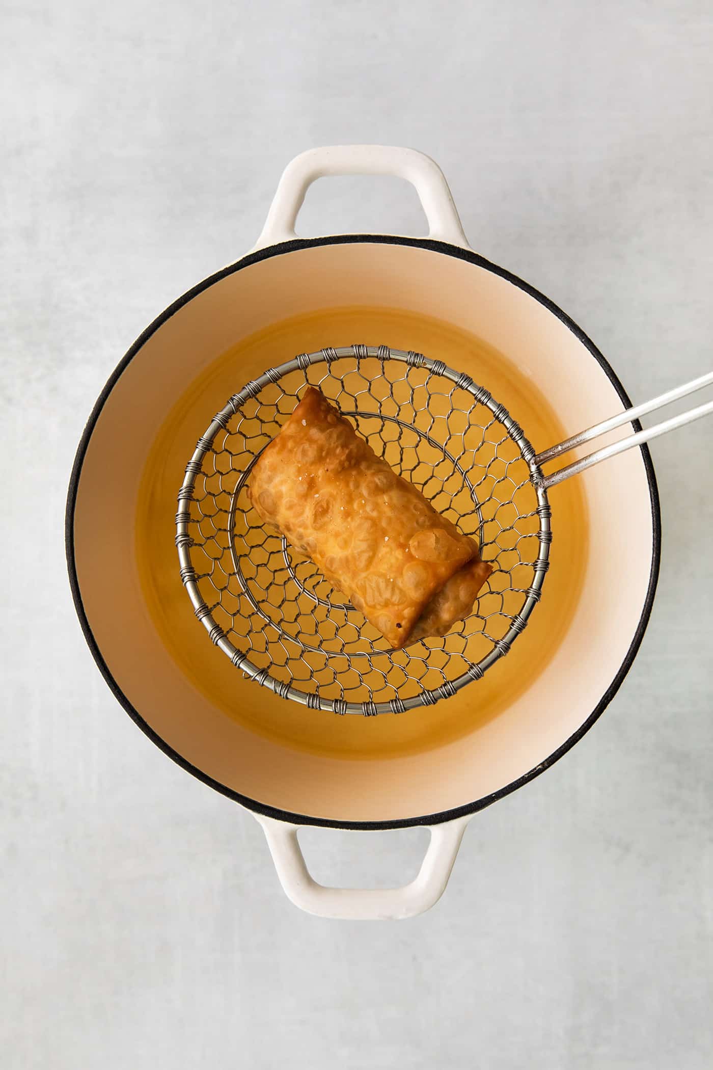 A spider strainer lifting an egg roll out of oil