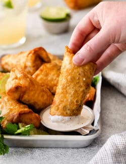 A hand dipping a southwest chicken egg roll into lime crema