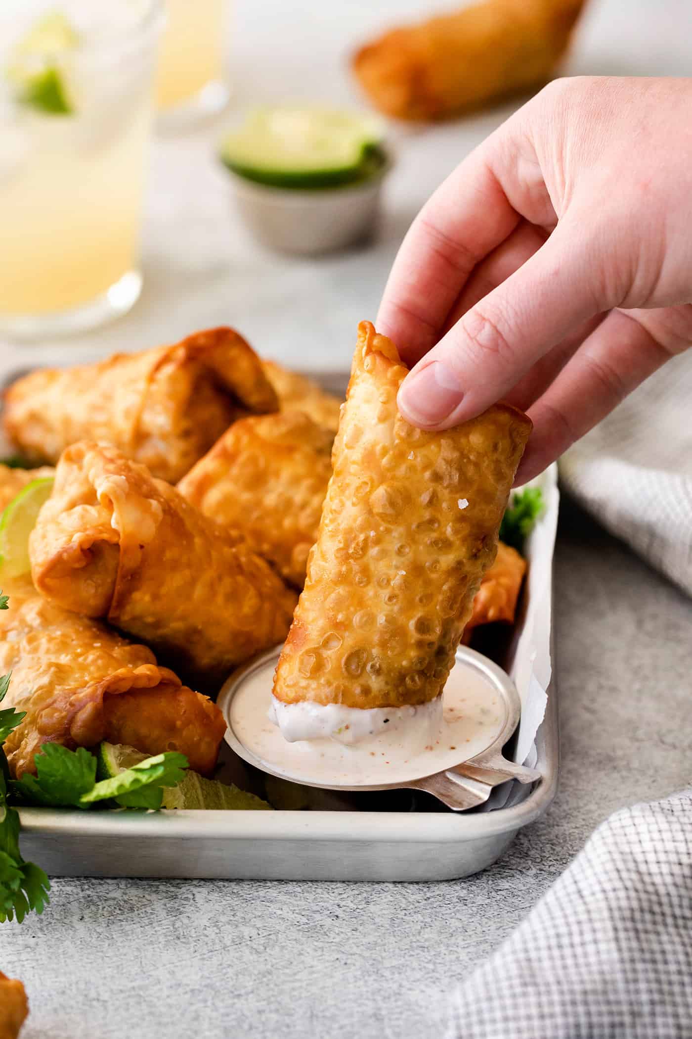 A hand dipping a southwest chicken egg roll into lime crema