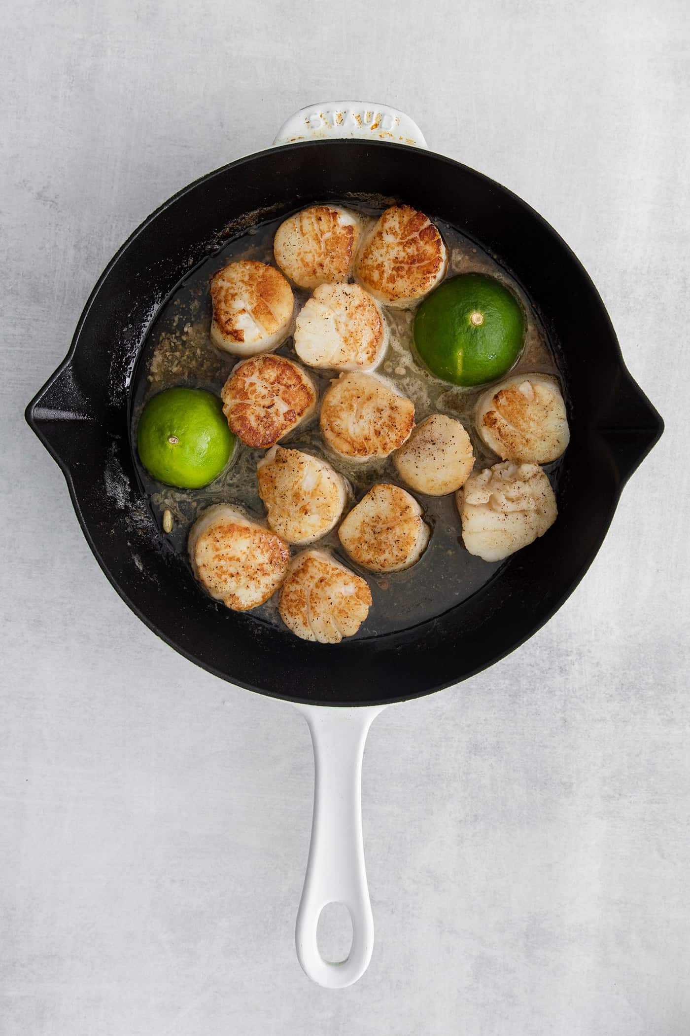 Seared scallops in a pan with lime halves