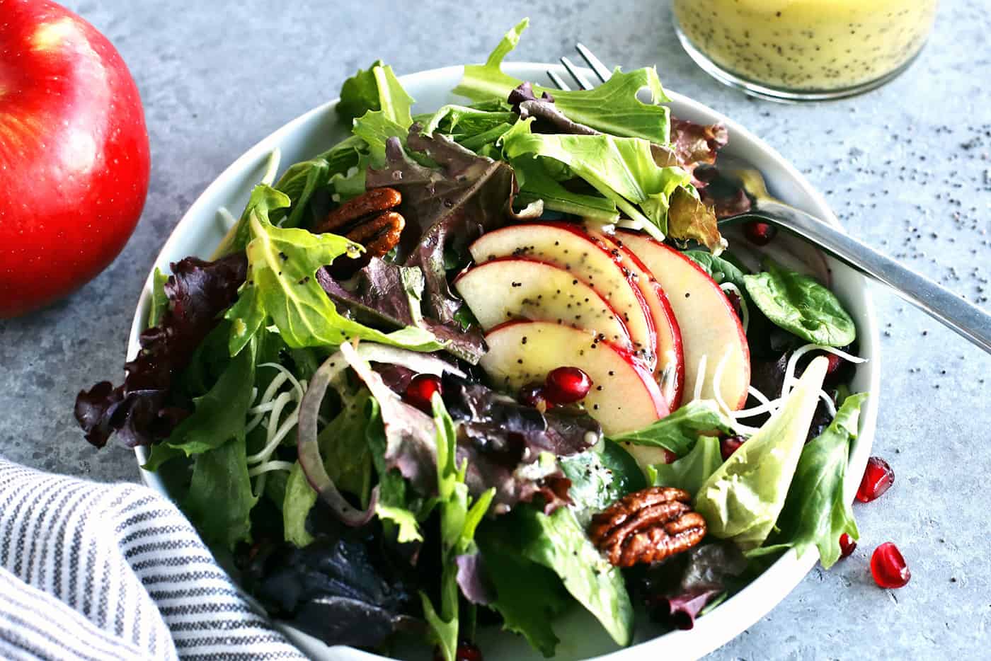 an individual plate of fresh salad greens with sliced apples and pecans