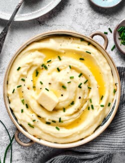 A large bowl of mashed potatoes with buttermilk, topped with melted butter and chives