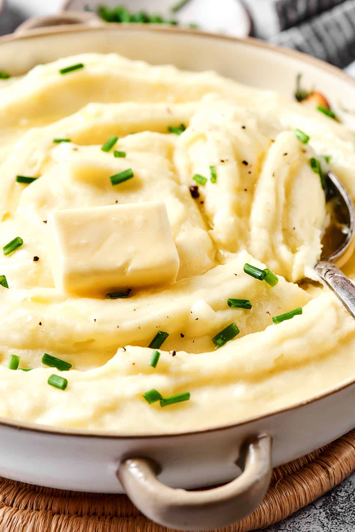 A spoon stirring buttermilk mashed potatoes topped with butter