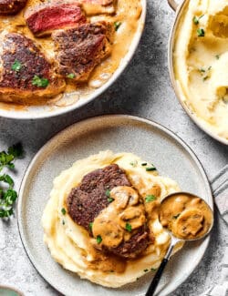 Steak Diane in a skillet, mashed potatoes in a pot, and an individual plate of mashed potatoes with Steak Diane