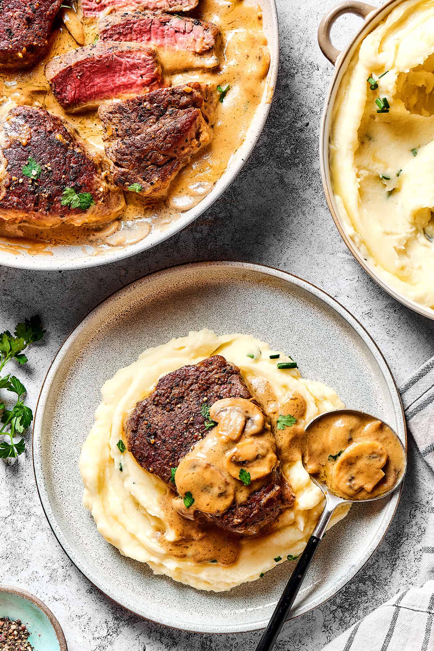 Steak Diane in a skillet, mashed potatoes in a pot, and an individual plate of mashed potatoes with Steak Diane