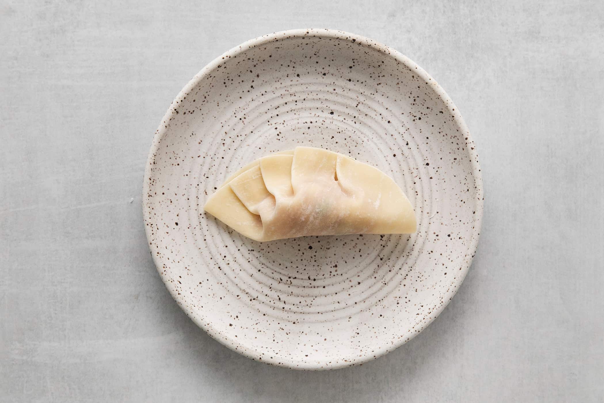 a potsticker on a plate, partially pleated