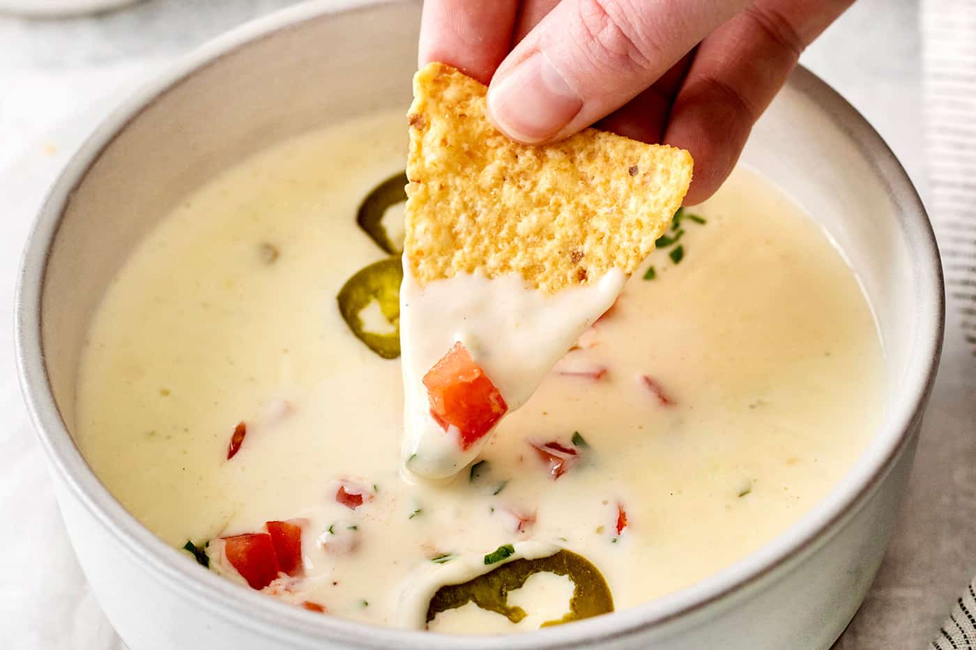 A hand dipping a chip into a bowl of queso blanco