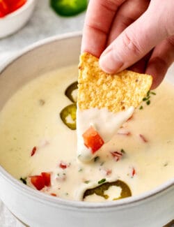 A hand dipping a tortilla chip into queso blanco