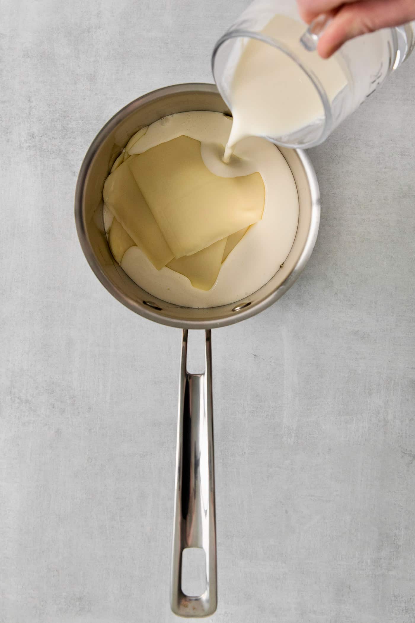 Heavy cream being poured over slices of American cheese in a saucepan
