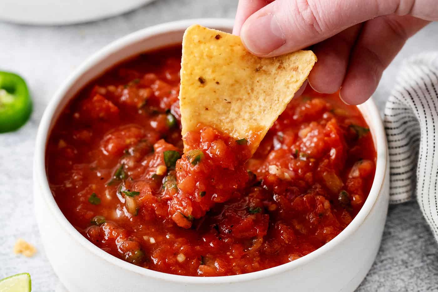 A hand dipping a tortilla chip into restaurant style salsa
