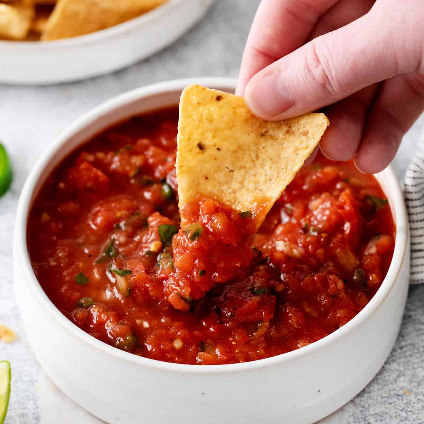 A hand dipping a chip into salsa