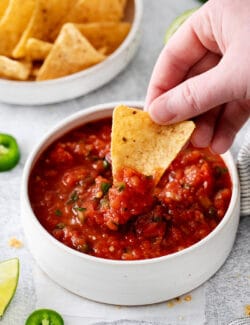 A hand dipping a chip into restaurant style salsa