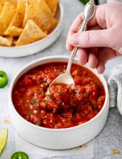 A hand holding a spoon in a bowl of restaurant style salsa