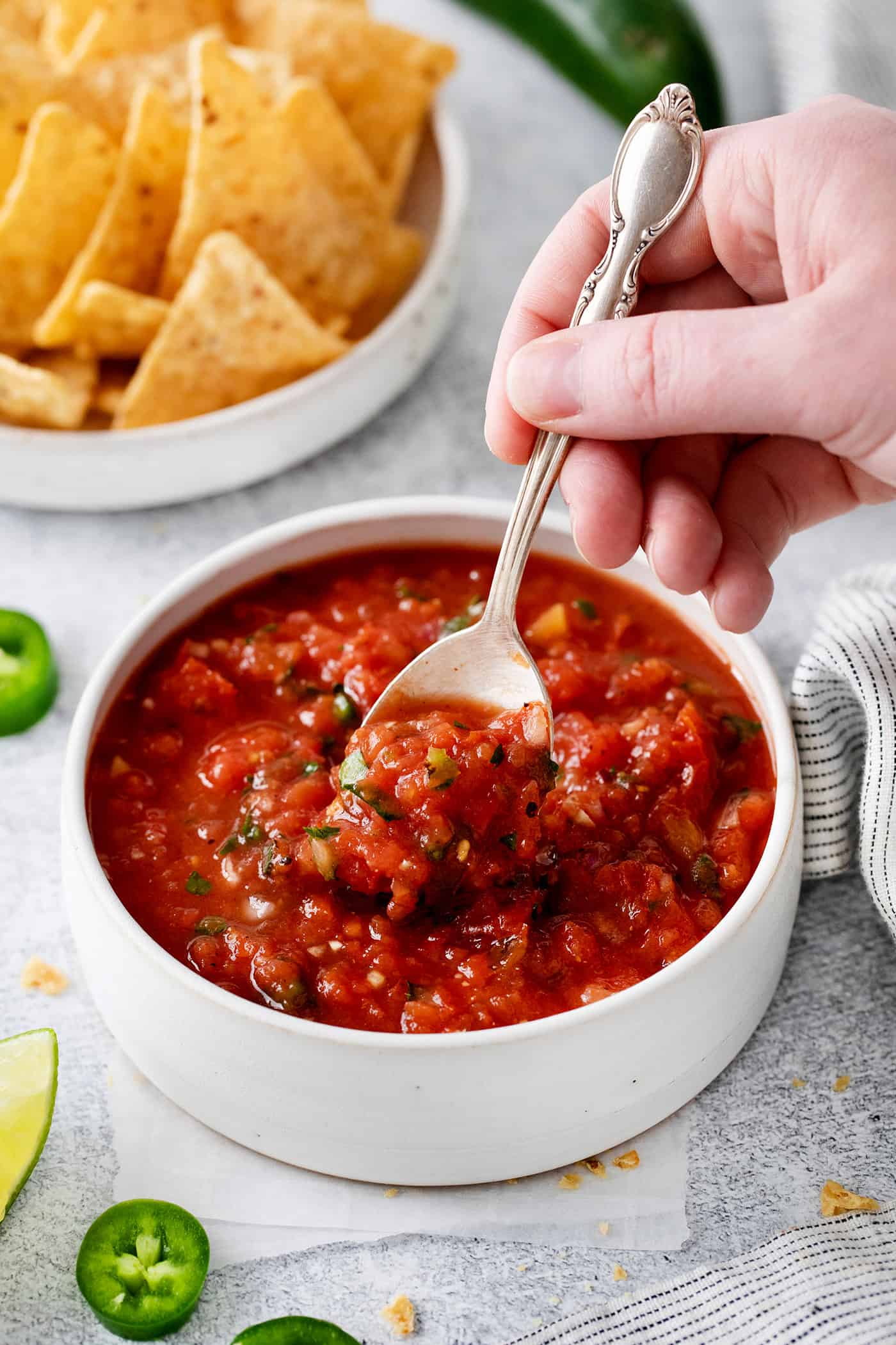 A hand holding a spoon in a bowl of restaurant style salsa