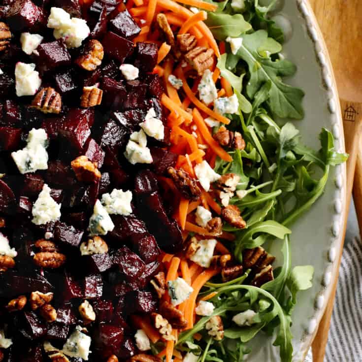 a large platter of salad with arugula, carrots, and roasted beets