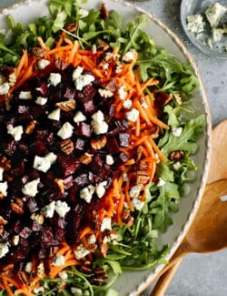 a large platter of salad with arugula, carrots, and roasted beets