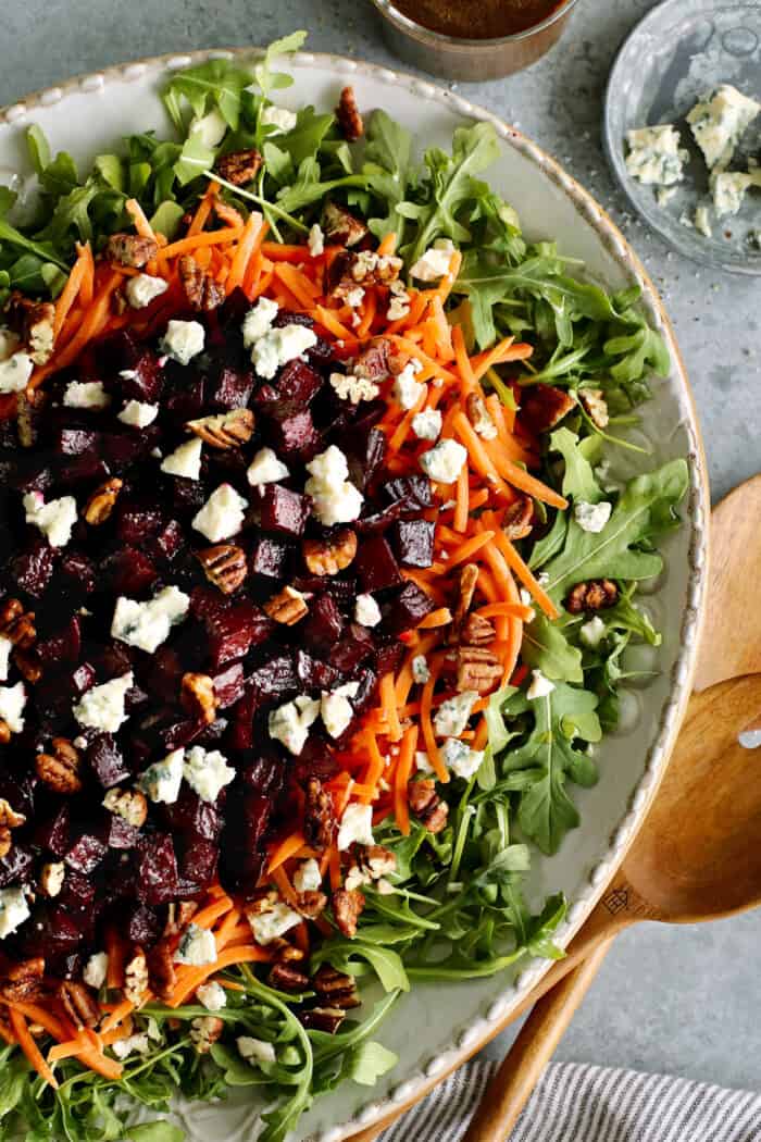 a large platter of salad with arugula, carrots, and roasted beets