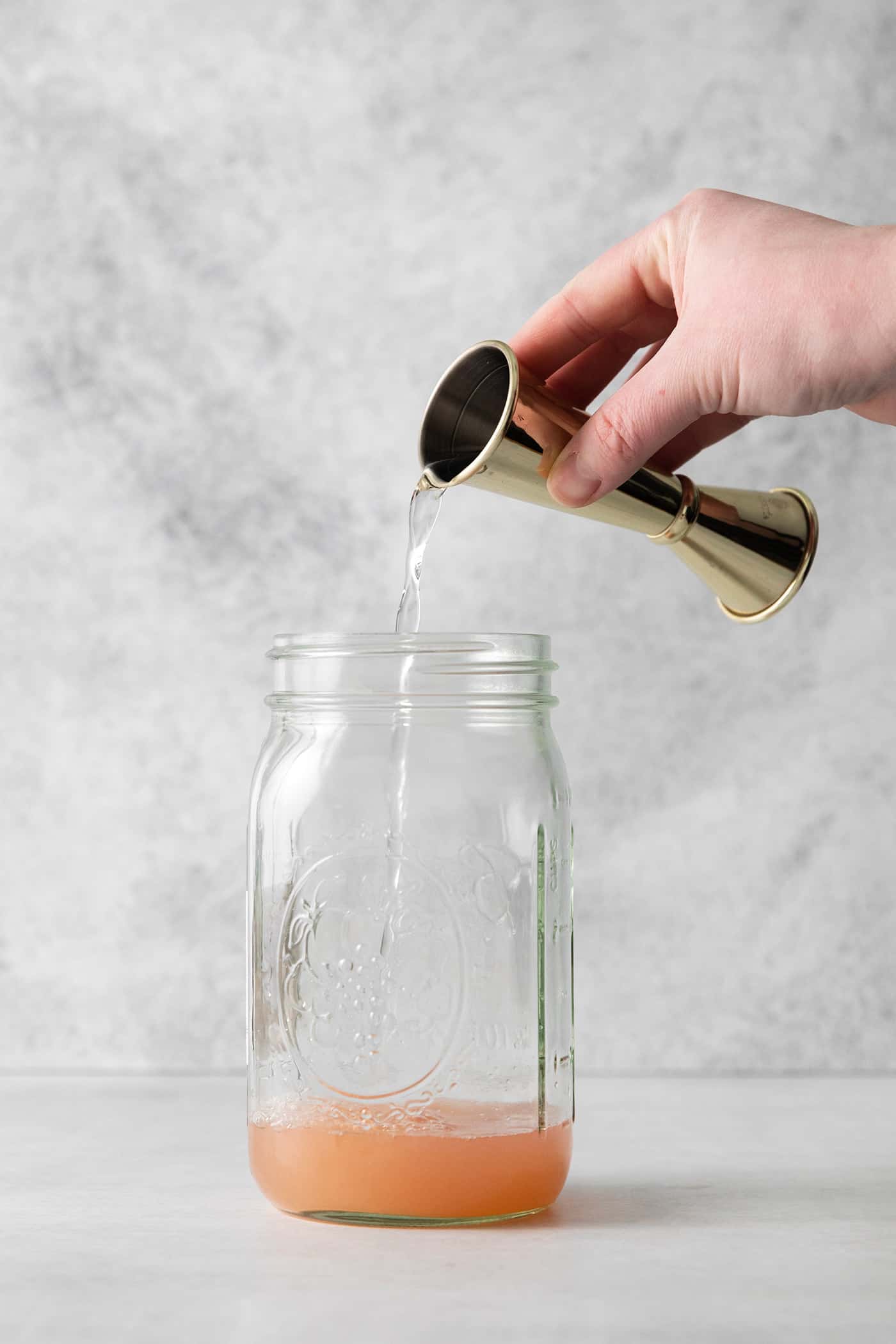 A hand pouring gin into a mason jar