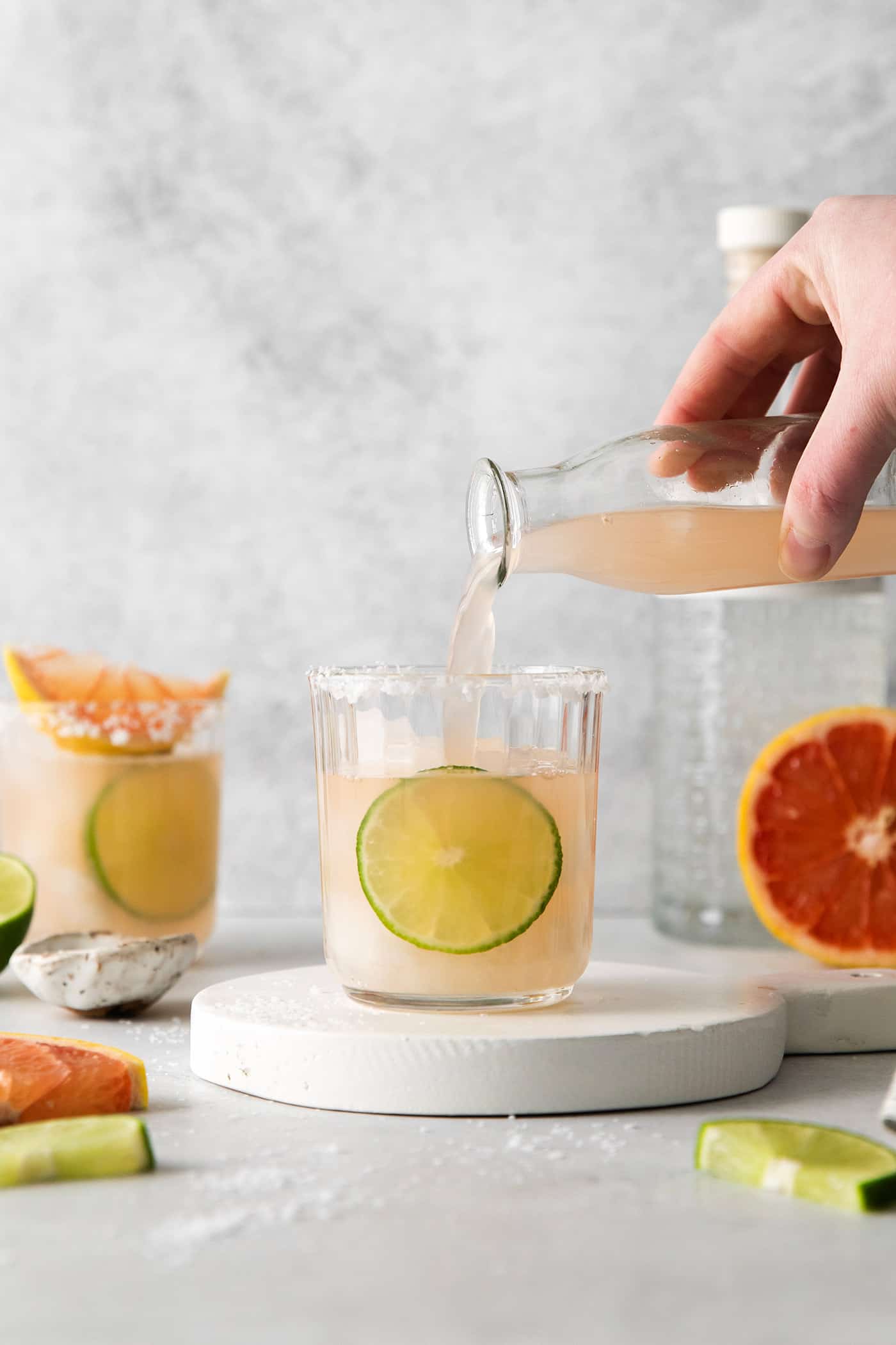A hand pouring grapefruit cocktail in a glass over ice