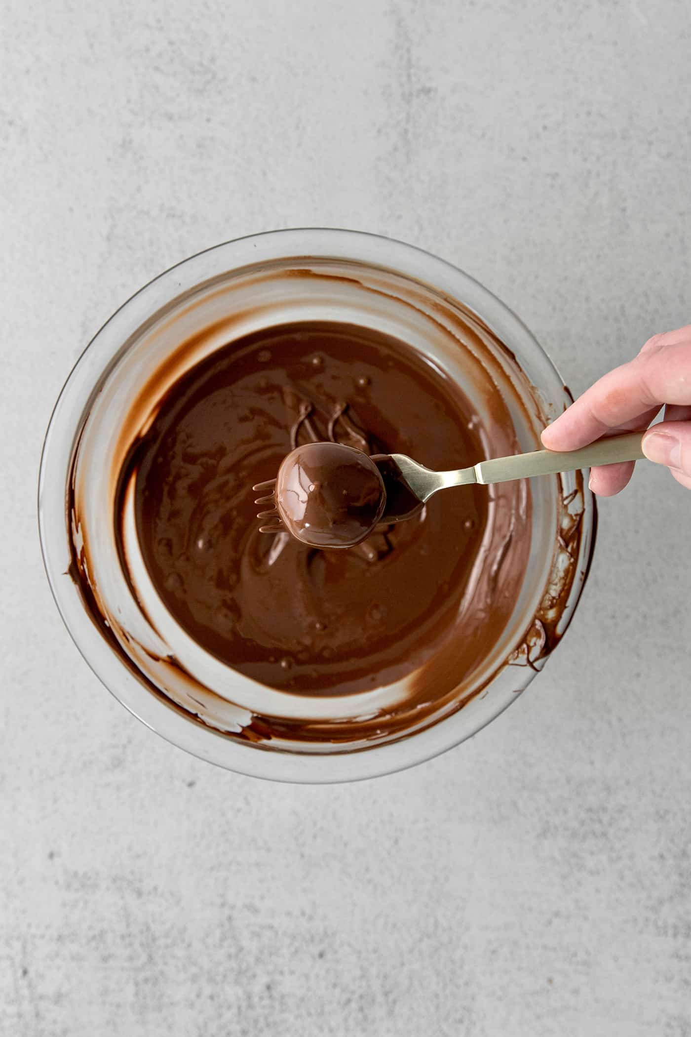 A truffle on a fork above a bowl of melted chocolate