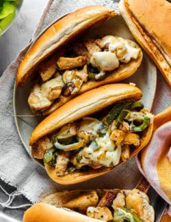 overhead photo of assembled sandwiches with hoagie rolls, chicken, green pepper, and melted cheese