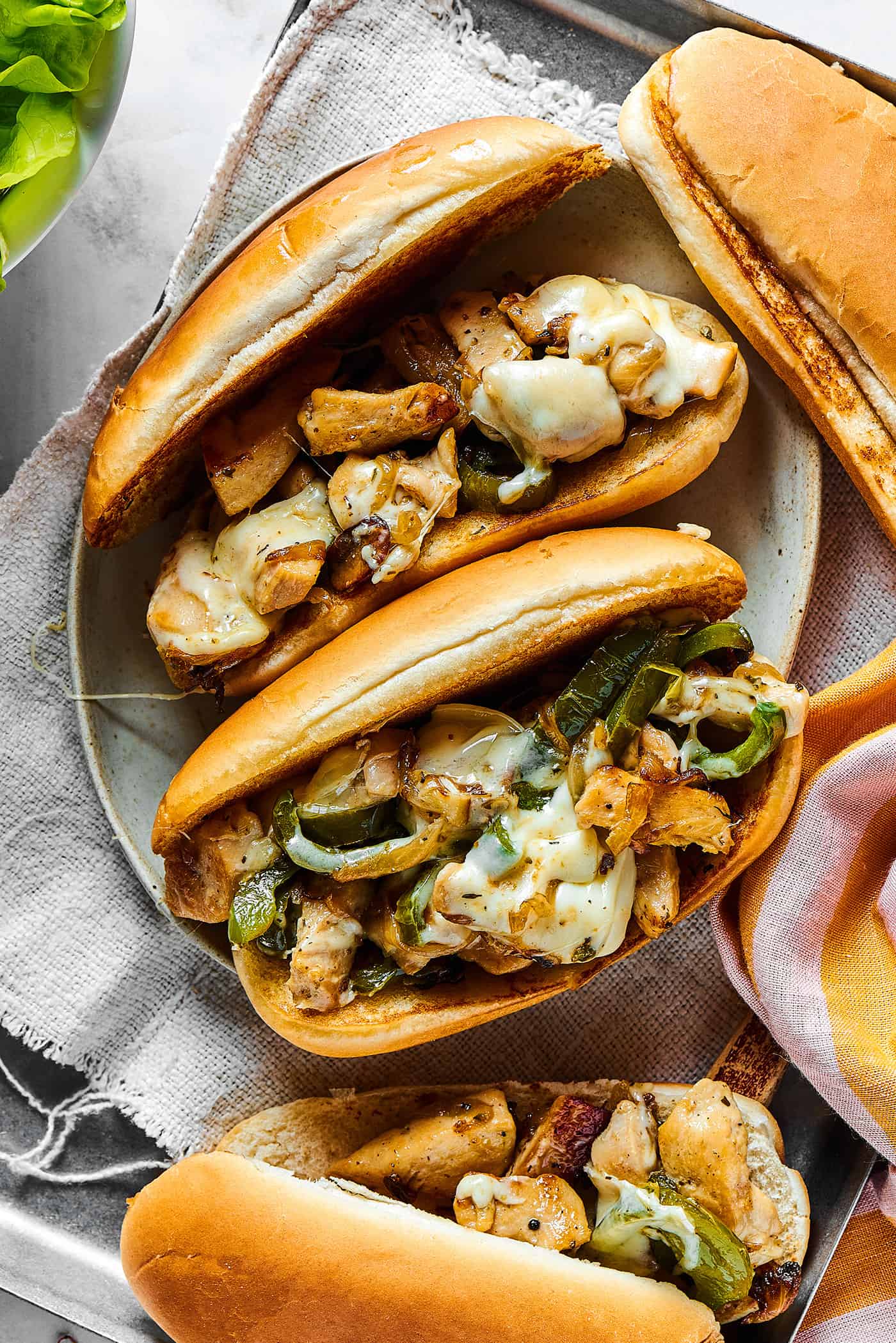 overhead photo of assembled sandwiches with hoagie rolls, chicken, green pepper, and melted cheese