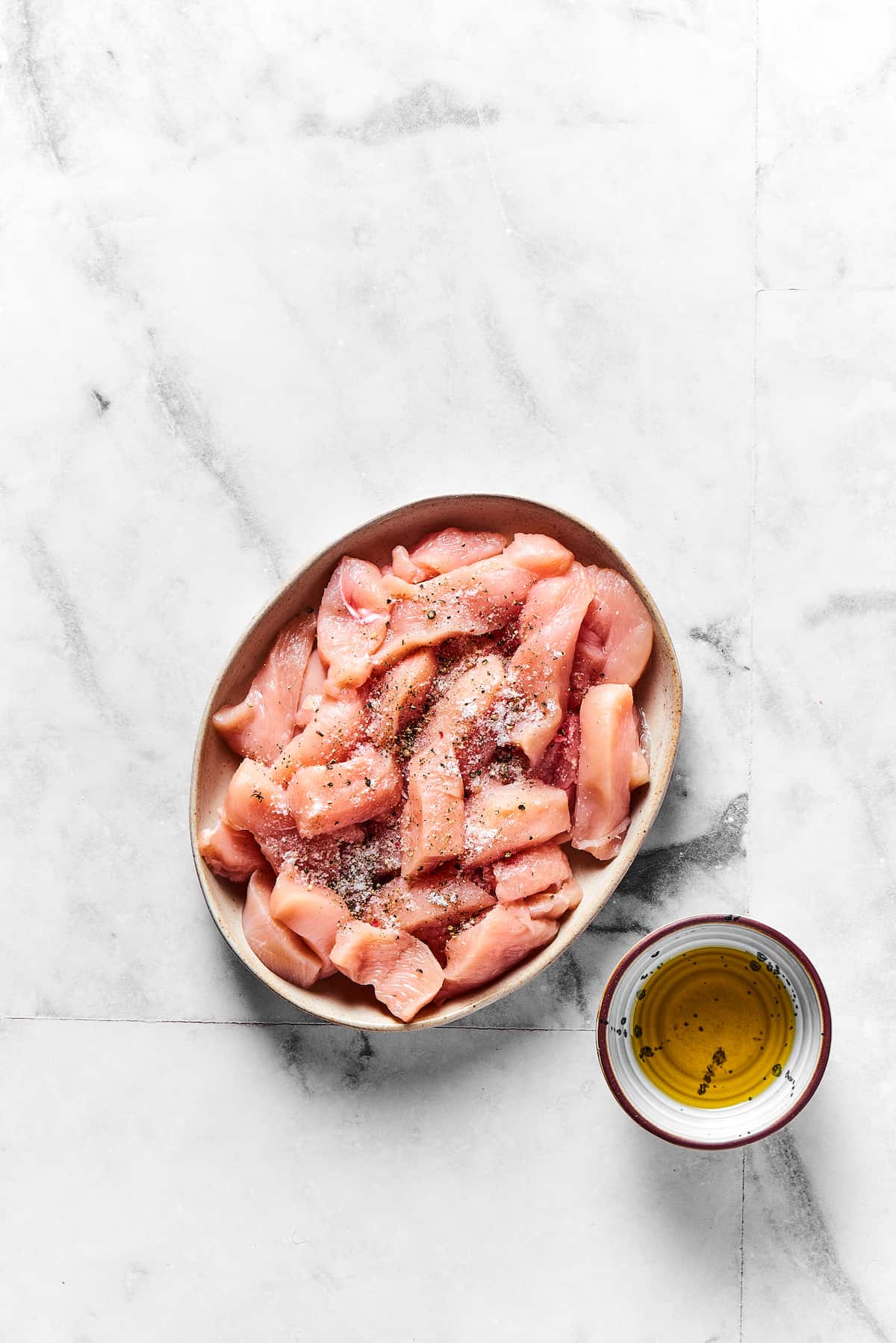 Strips of raw chicken breast next to a bit of olive oil