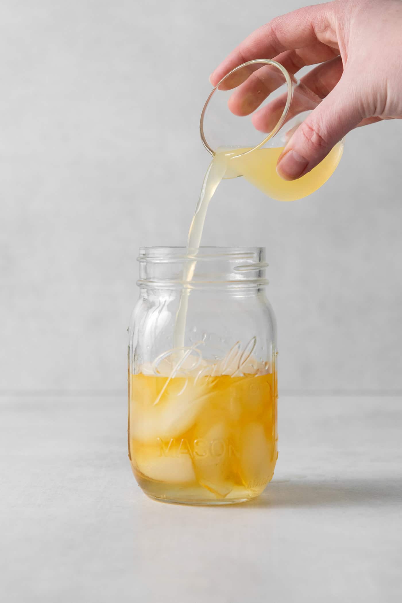 Lemon juice being poured into a mason jar with whiskey