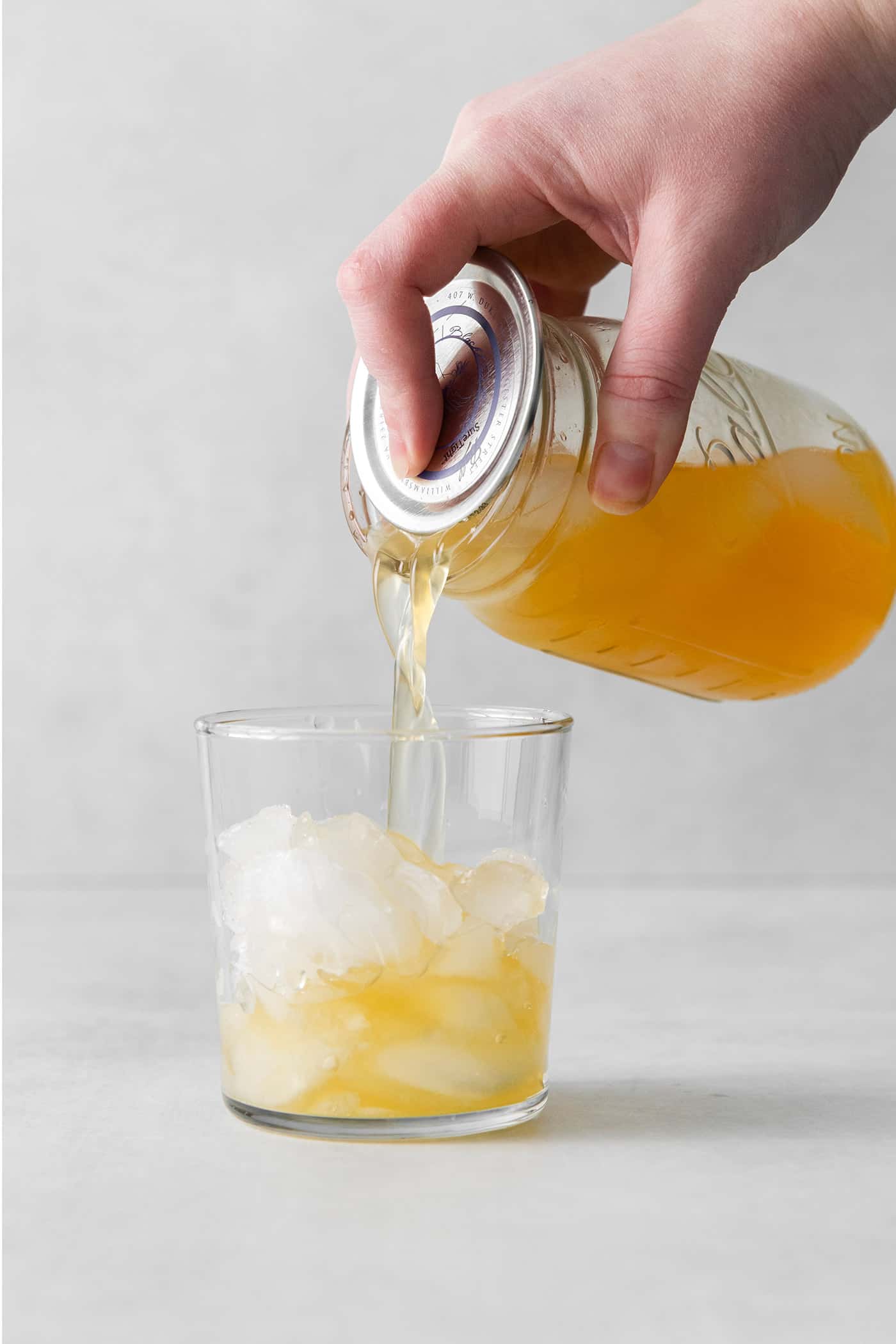 A sour cocktail being poured from a mason jar into a cocktail glass over ice