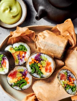 sushi burritos cut in half, on a platter with wasabi dip